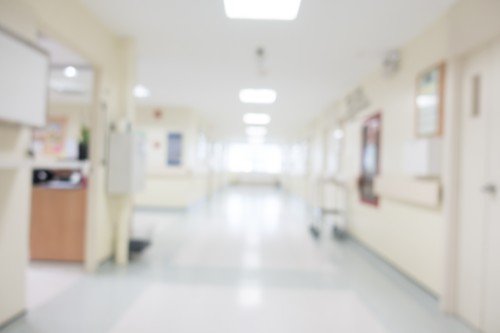 Blurred interior of a Hospital corridor with patient care areas, wall-mounted handrails, and overhead fluorescent lighting